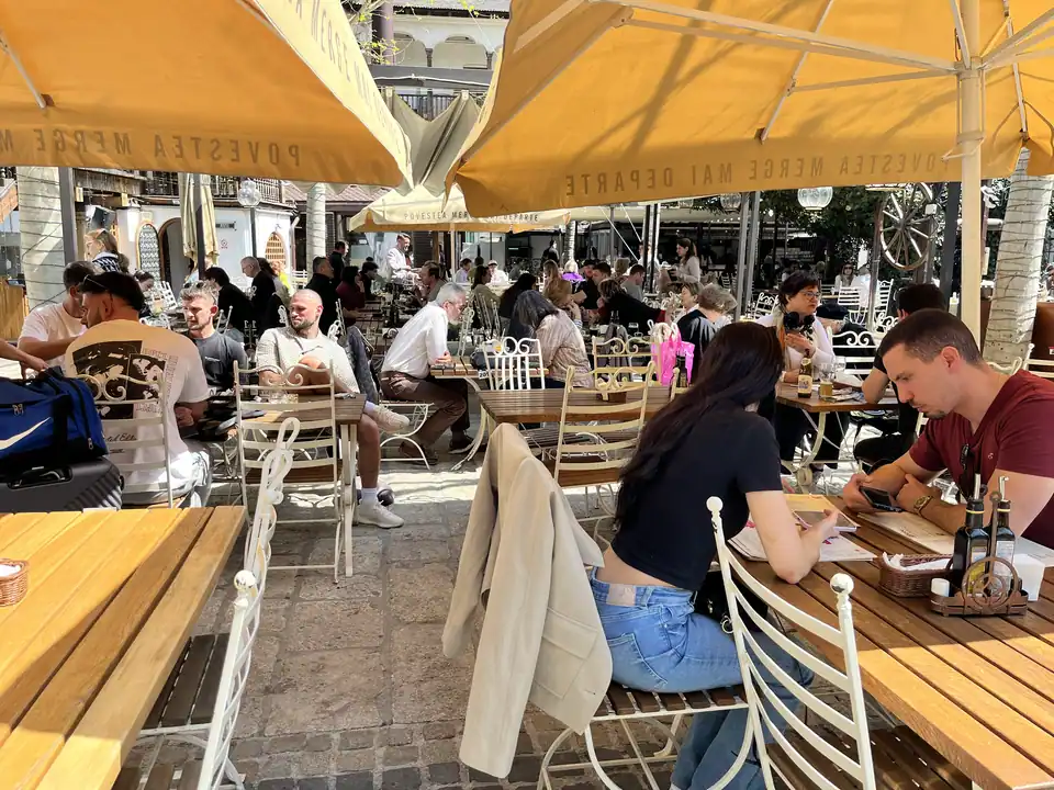 Diners seated beneath yellow umbrellas in Hanu’ lui Manuc’s outdoor courtyard.