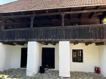 White rural house with a broad covered wooden balcony.