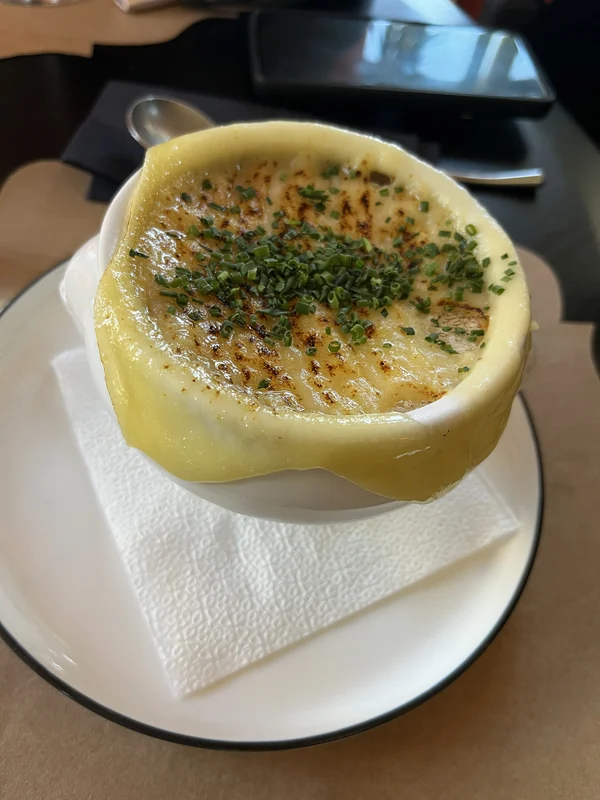 Soup topped with browned cheese and herbs in a yellow handled bowl