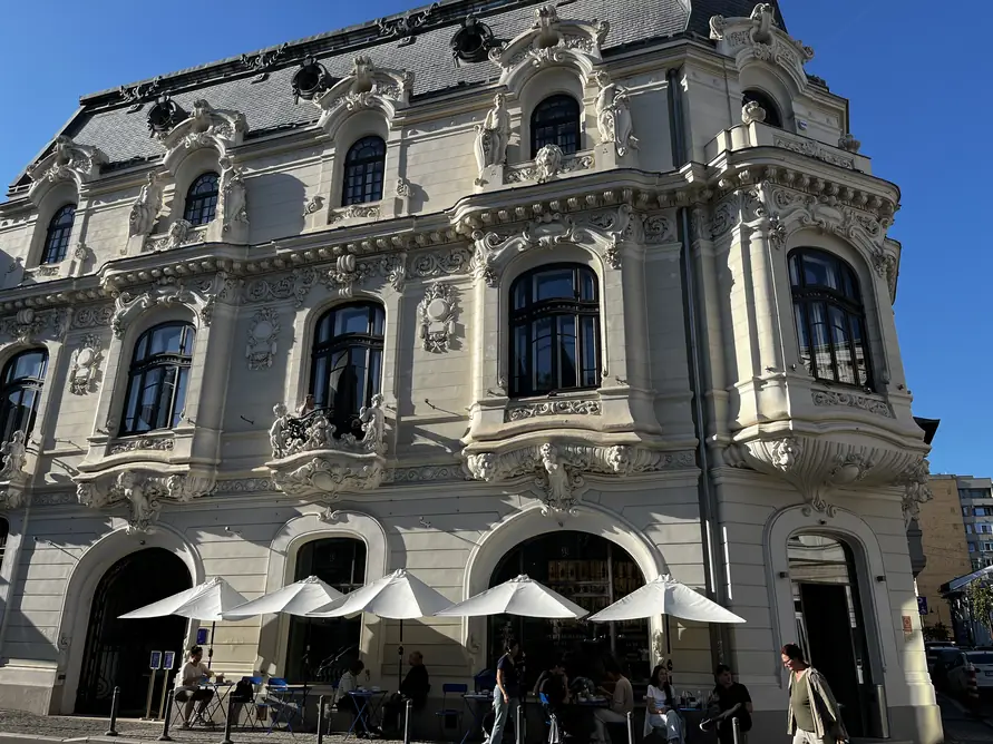 Ornate facade of Casa Mița Biciclista with pavement tables beneath white umbrellas