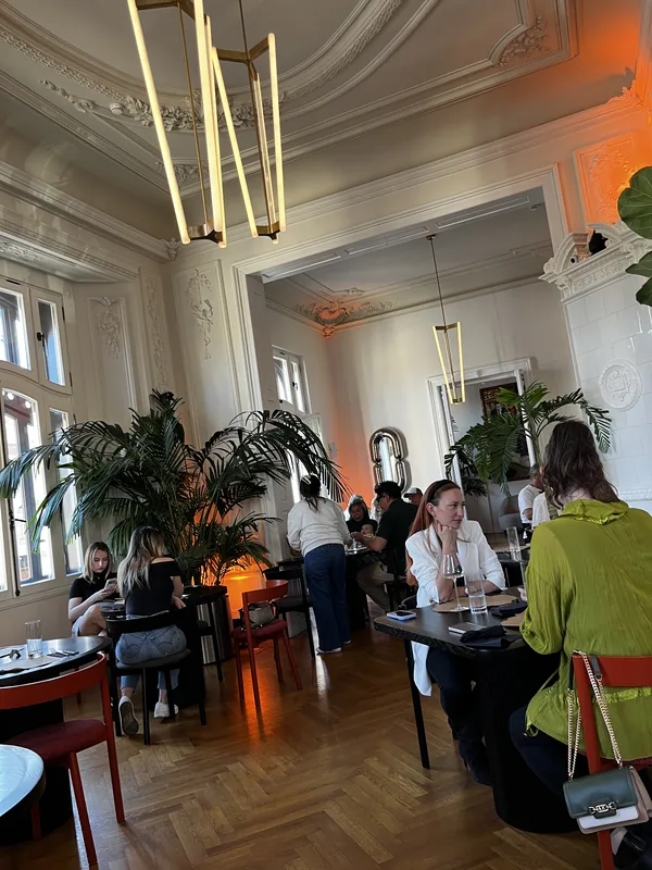 Dining tables, tall palms and ornate ceiling in the historic salon at Casa Mița Biciclista