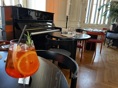 Orange drink on a salon table with a piano and tall windows in the background