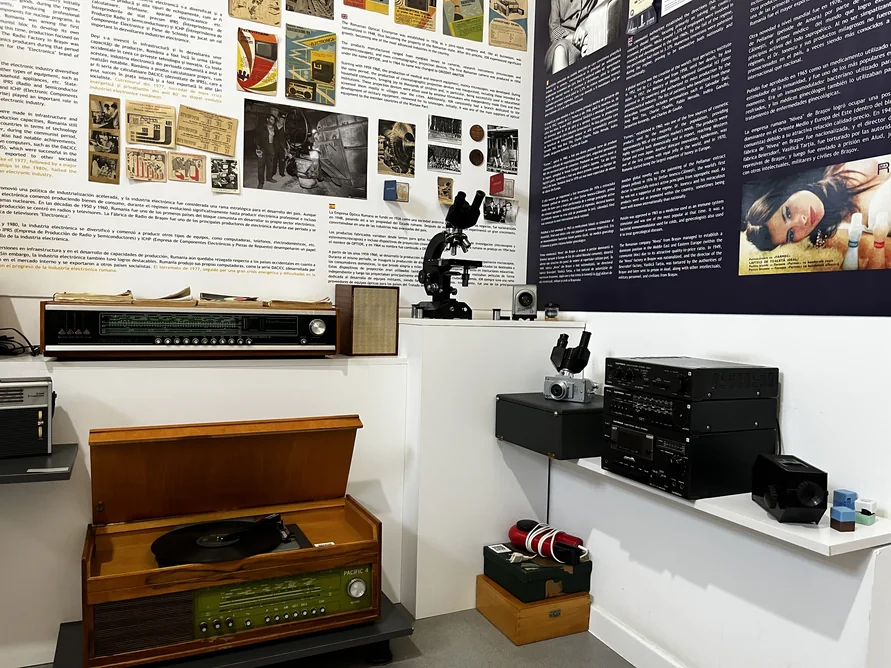 Wooden record player, radios, cameras and audio equipment beneath museum information panels.