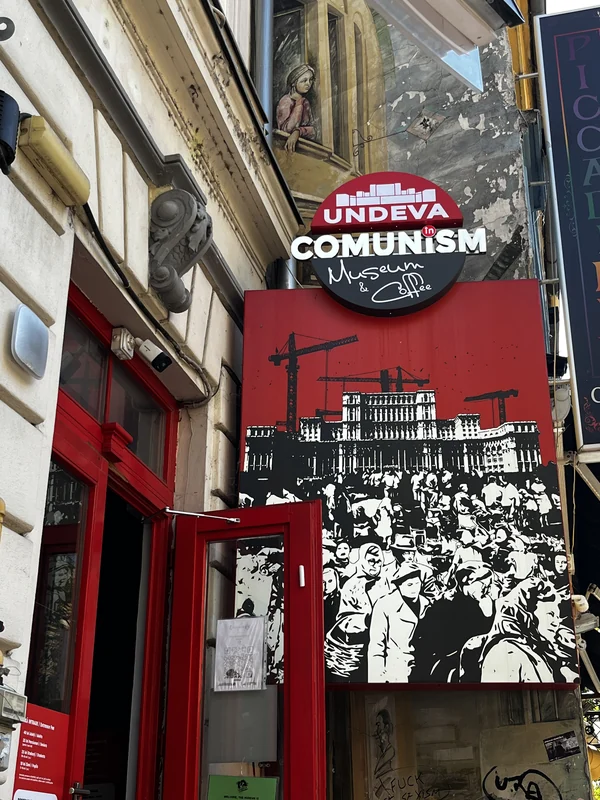 Red entrance door beneath the Undeva în Comunism Museum and Coffee sign on Soarelui Street.